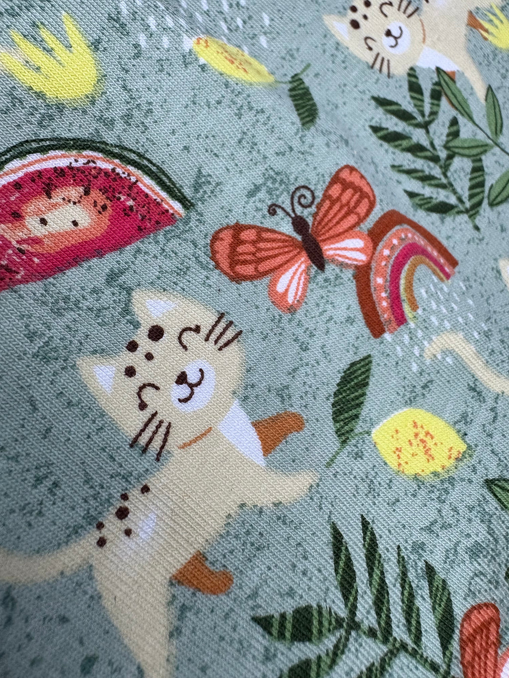Fabric with cat-themed design featuring cats, butterflies, and plants on a green background.