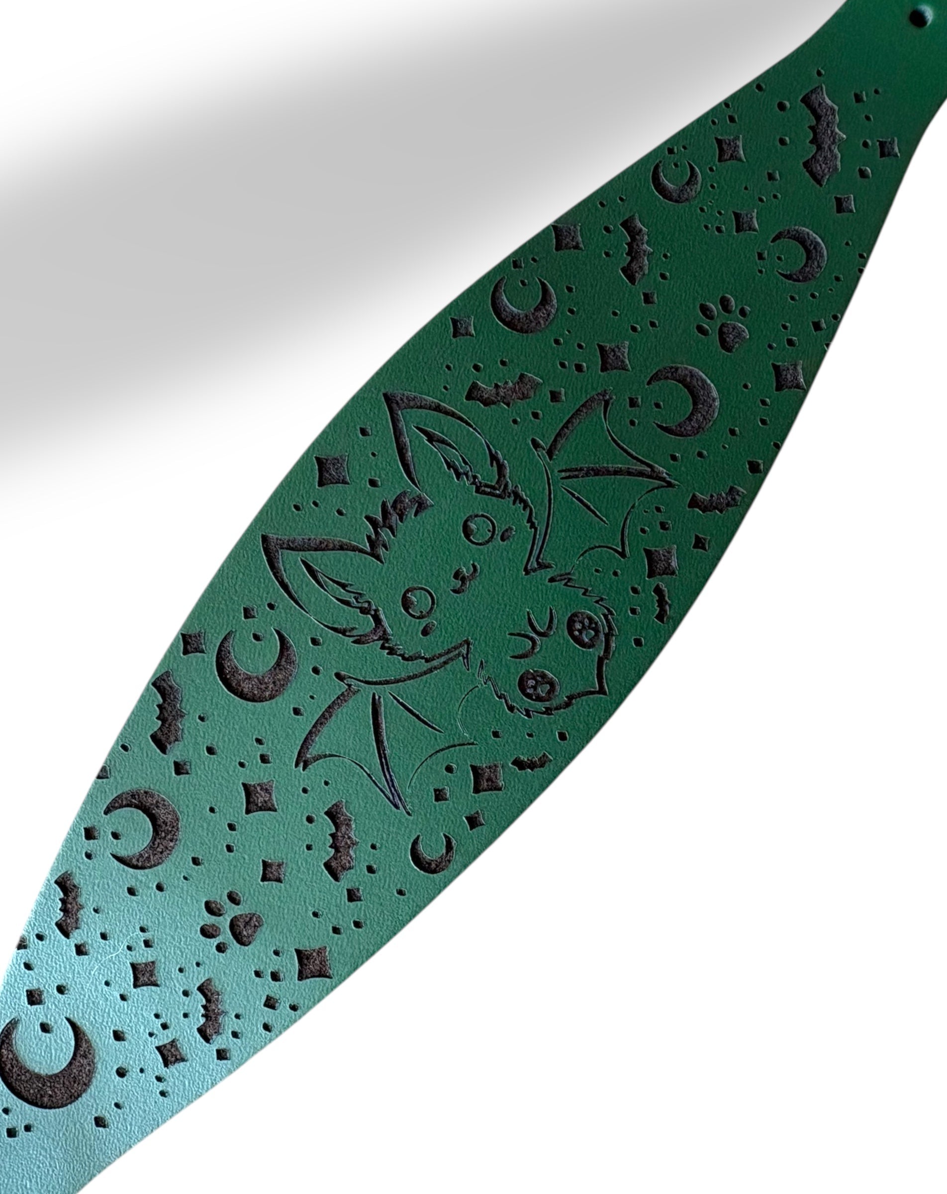 Green leather guitar strap with engraved design on a white background