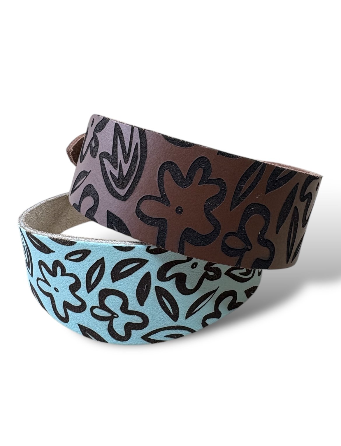 Two patterned belts, one brown with black floral design and one blue with black floral design, on a white background.