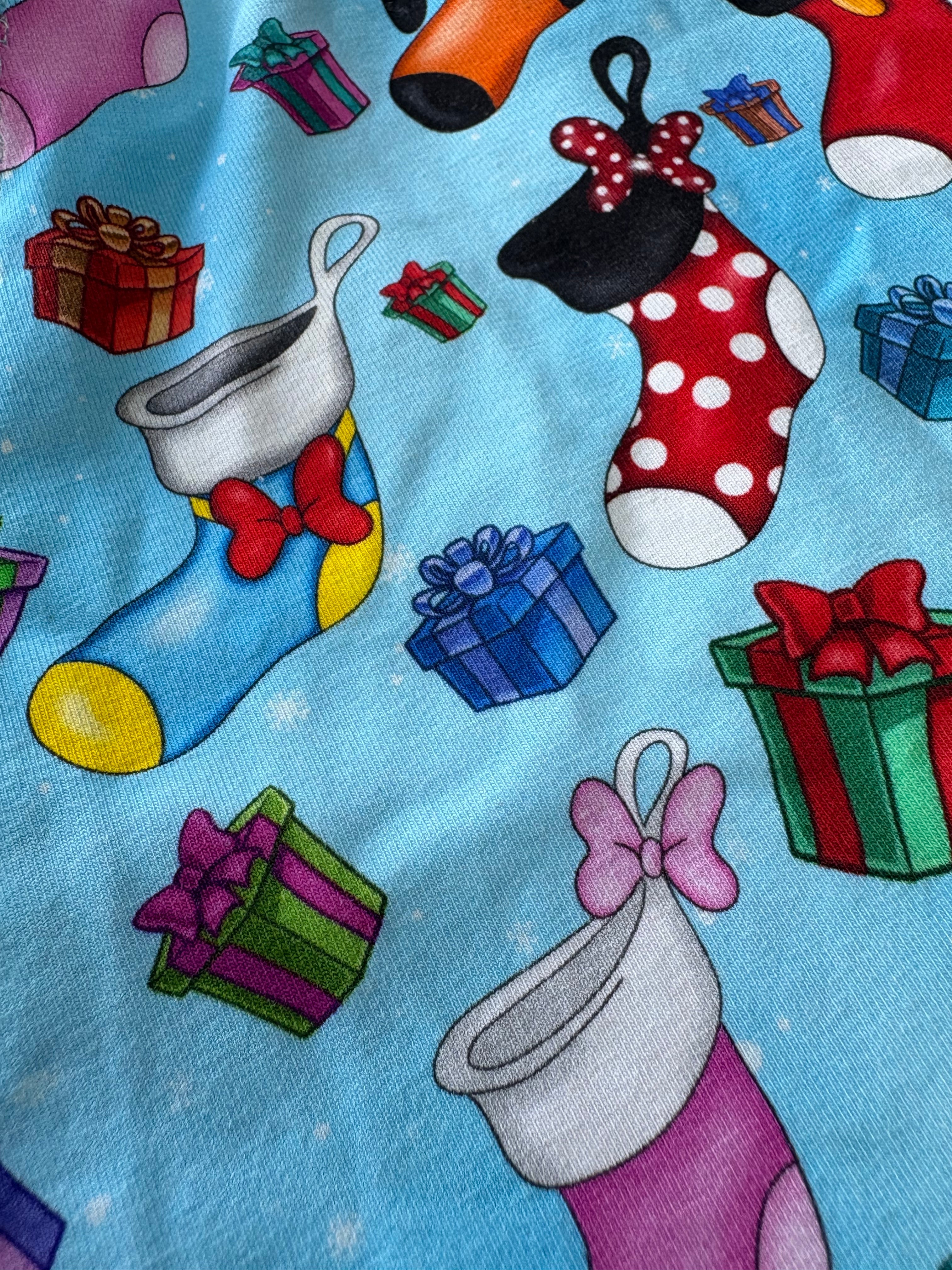 Colorful fabric with Christmas-themed designs including stockings, presents, and bows on a blue background.