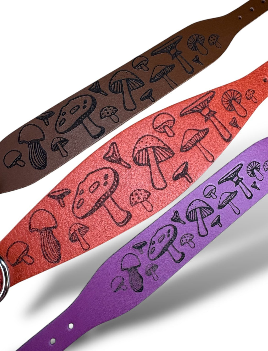 Three guitar straps with mushroom pattern in brown, red, and purple on a white background