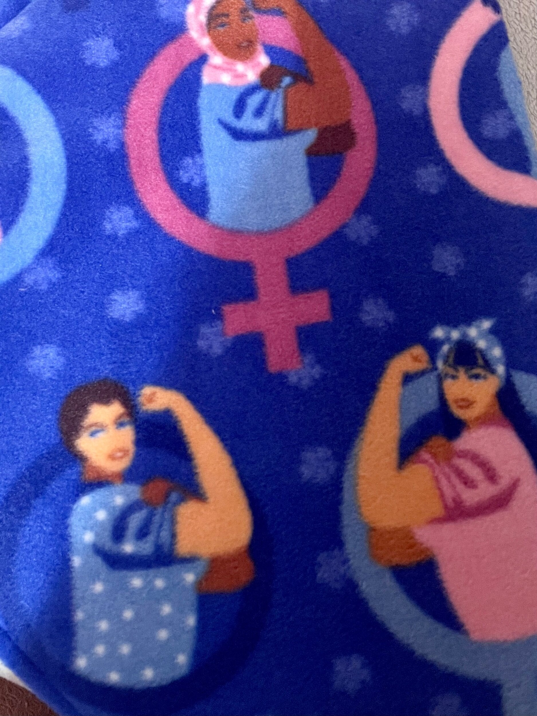 Patterned fabric with female gender symbols and illustrated women on a blue background.