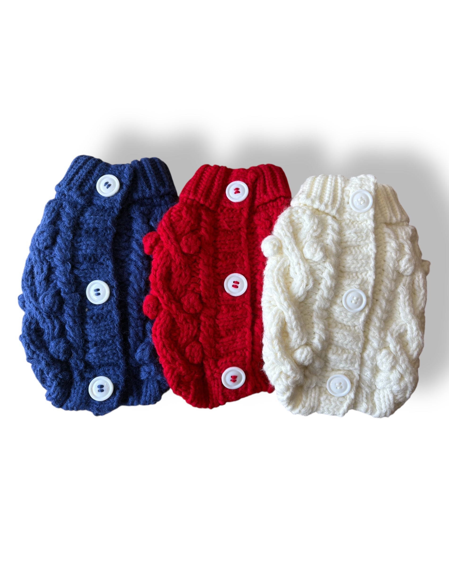 Three knitted dog sweaters in blue, red, and white on a white background