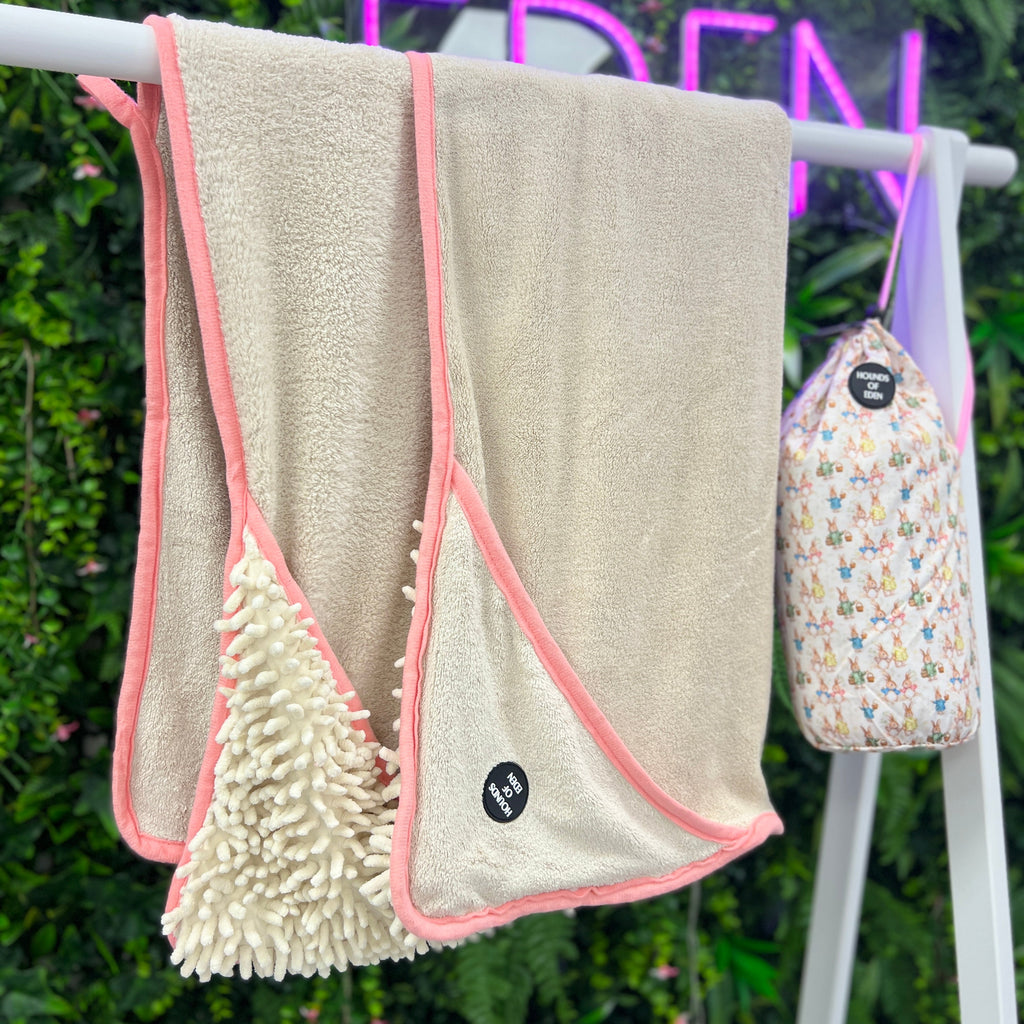 Beige towel with pink trim hanging on a rack with a floral pouch in the background.
