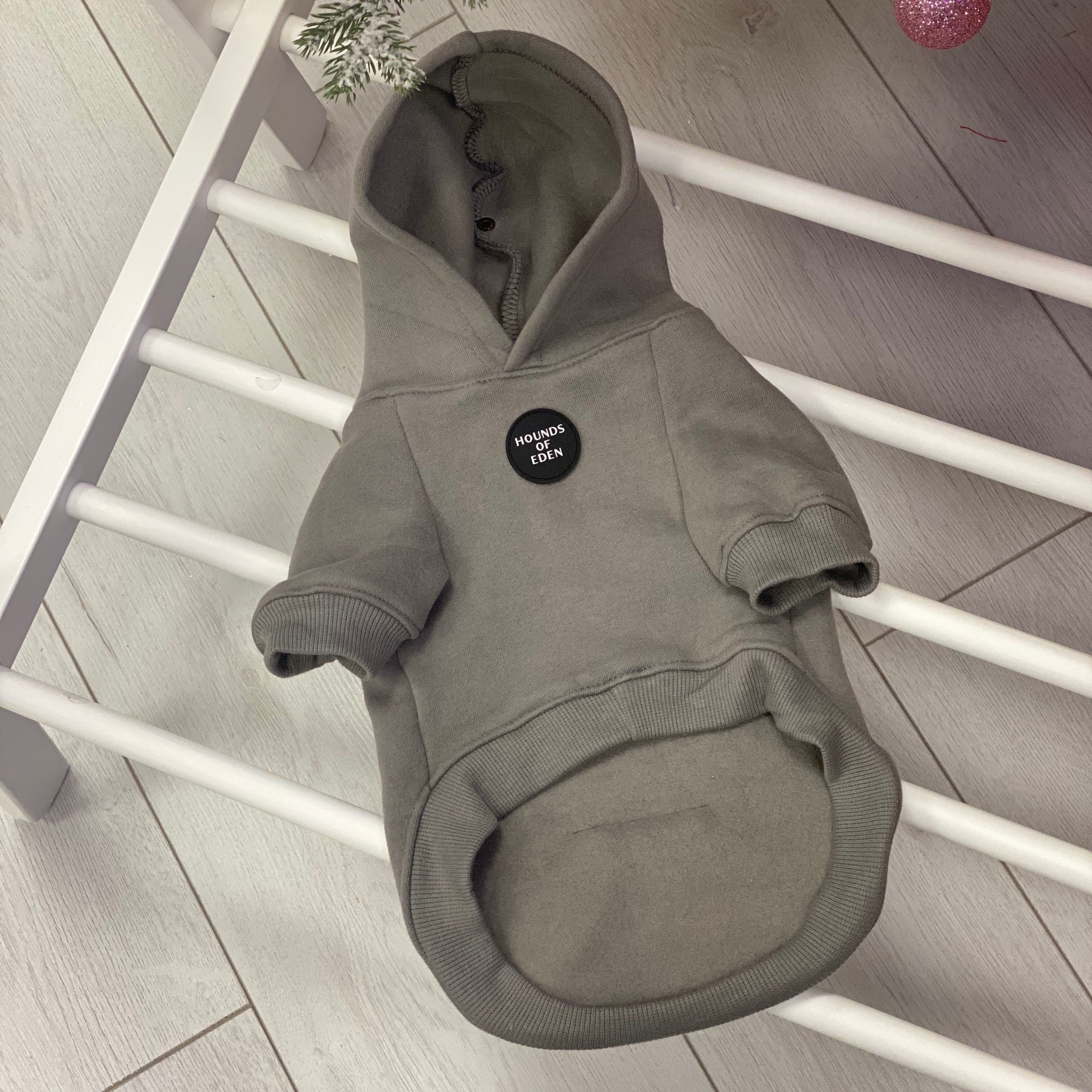 Gray dog hoodie with a black patch on a white wooden floor