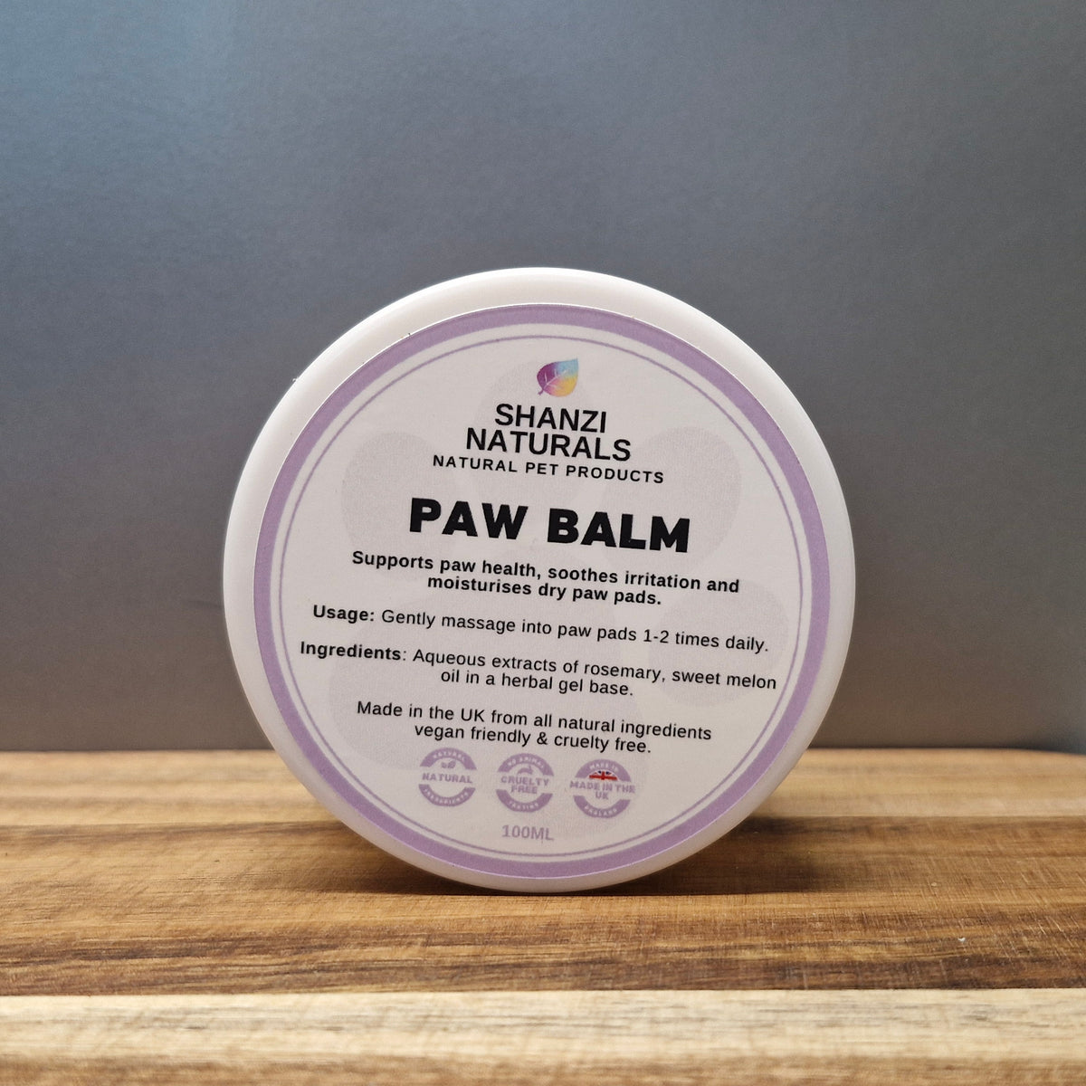 Shanzi Naturals Paw Balm container on a wooden surface with a gray background