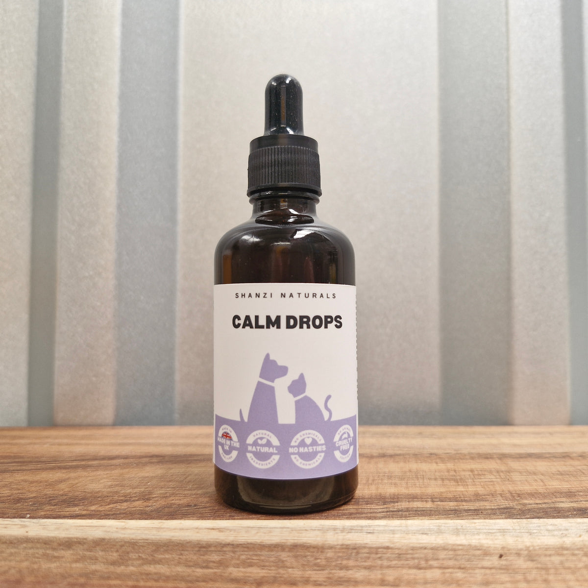 Bottle of 'Calm Drops' on a wooden surface with a striped background
