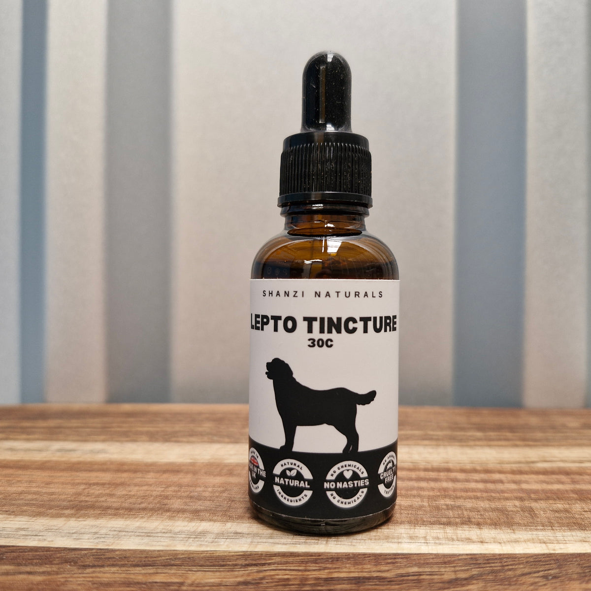 Bottle of Shanzi Naturals Lepto Tincture 30c on a wooden surface with a striped wall background