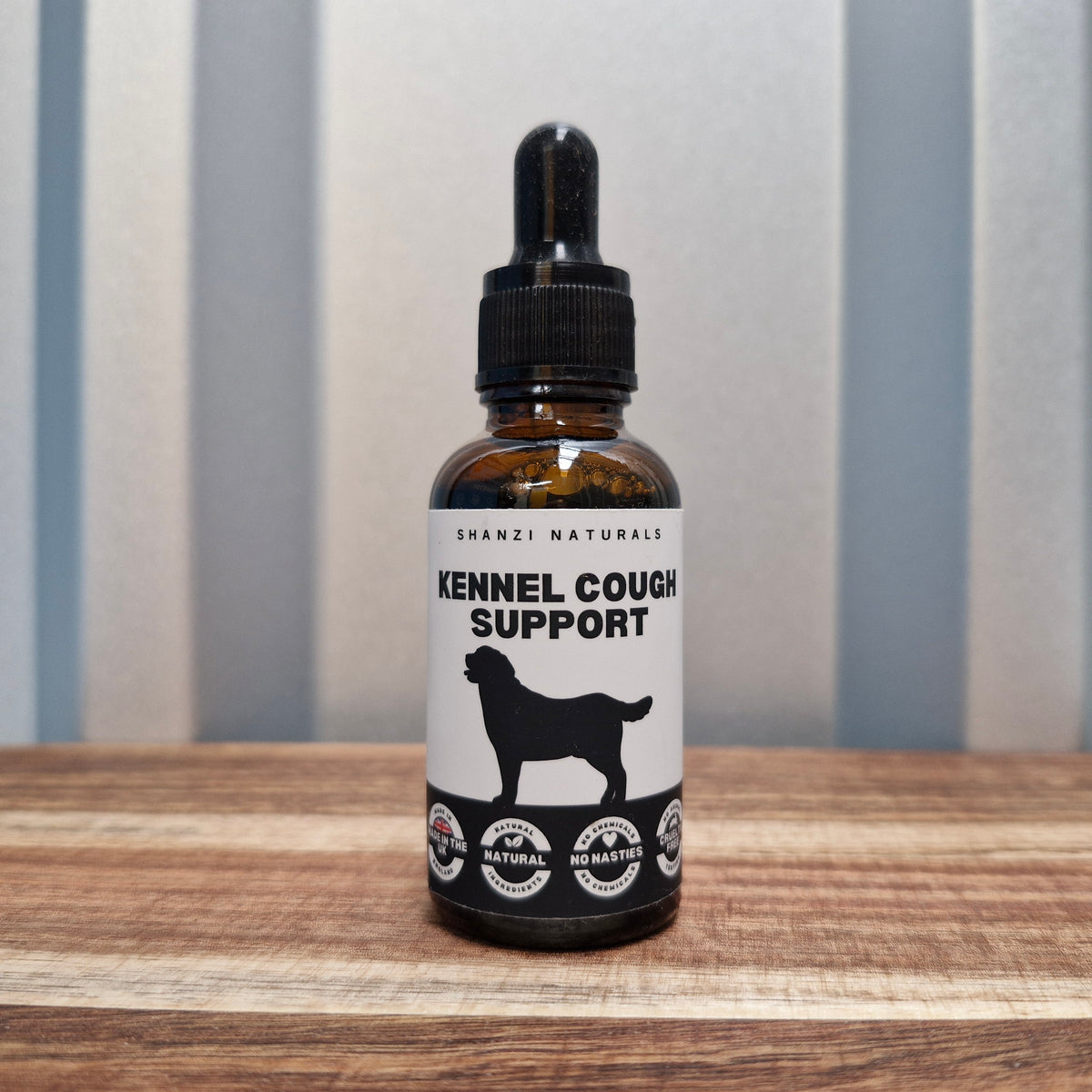 Bottle of Shanzi Naturals Kennel Cough Support on a wooden surface with a striped background
